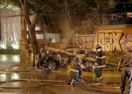Motorista foge após carro colidir contra poste, pegar fogo e matar passageiro